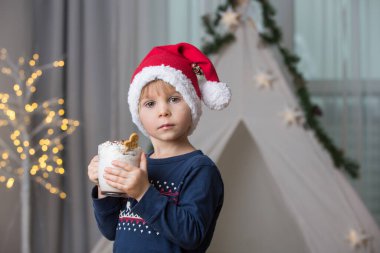 Güzel sarışın çocuk, çocuk, sıcak kakao içiyor. Yanında krema ve Noel süsü var.