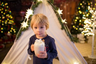 Güzel sarışın çocuk, çocuk, sıcak kakao içiyor. Yanında krema ve Noel süsü var.