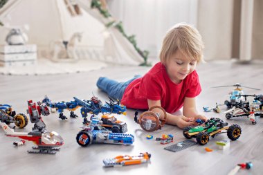 Tatlı çocuk, sarışın çocuk, Colofrul plastik bloklarla oynuyor, inşaat oyuncakları, araba ve uçak yapıyor.