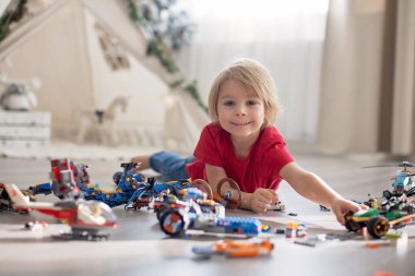 Tatlı çocuk, sarışın çocuk, Colofrul plastik bloklarla oynuyor, inşaat oyuncakları, araba ve uçak yapıyor.