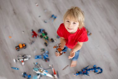 Tatlı çocuk, sarışın çocuk, Colofrul plastik bloklarla oynuyor, inşaat oyuncakları, araba ve uçak yapıyor.