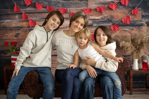 Cute family portrait, mother and three boys with valentine decoration, love, flowers, sitting on armchair with frame in studio