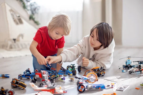 Cute toddler child and older brother, blond boy, playing with colofrul plastic blocks, construction toys, making cars and planes