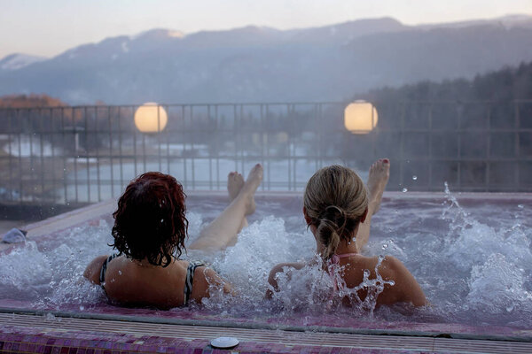 People, enjoying whirlpool and saunta after day of skiing, relaxing in nice warl whirlpool outdoor, splendid view on a sunset
