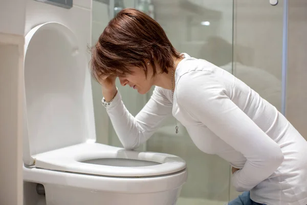 Woman, girl, experiencing sickness, vomiting, pregnancy, poisoning and morning discomfort, sitting over the toilet