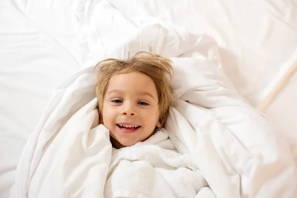 金发碧眼的小孩 对着摄像机笑着 在床上洗完澡后裹上毛巾 — 图库照片
