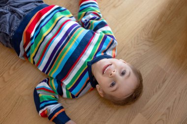 Cute child, blond boy, lying on the floor at home, looking at camera, shot from above