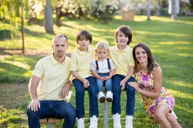 Güzel bir aile, anne, baba ve üç çocuk. Güneşli bir bahar akşamında aile fotoğrafı çektiren çocuklar. Çiçek açan güzel bir bahçe. Ebeveynler ve çocuklar eğleniyor.