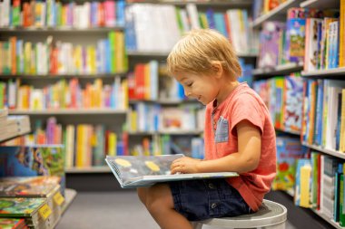 Cute preschool child, sitting in a bookstore, looking at books on summer day
