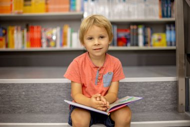 Cute preschool child, sitting in a bookstore, looking at books on summer day