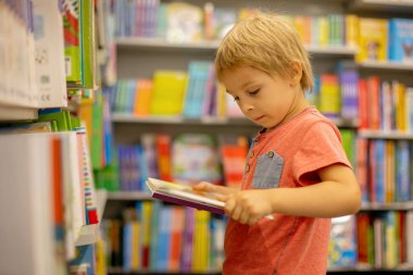 Cute preschool child, sitting in a bookstore, looking at books on summer day