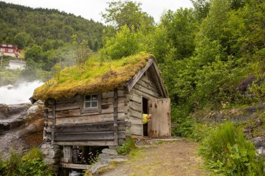 Amazing little wooden small house next to a waterfall on the dock of Hellesylt, child playing in the house, looking out of the window