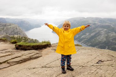 Family, enjoying the hike to Preikestolen, the Pulpit Rock in Lysebotn, Norway on a rainy day, toddler climbing with his pet dog the one of the most scenic fjords in Norway
