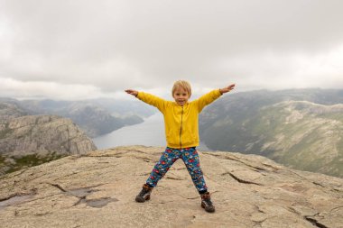 Family, enjoying the hike to Preikestolen, the Pulpit Rock in Lysebotn, Norway on a rainy day, toddler climbing with his pet dog the one of the most scenic fjords in Norway