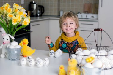 Küçük çocuk, siyah kalemle paskalya yumurtalarına komik ifadeler çiziyor.