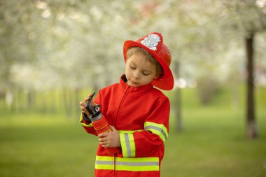Little toddler child with fireman costume in park, pretending to be real fireman, playing on sunset