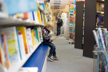 Bir kitapçıda oturup kitap okuyan sevimli küçük bir çocuk.