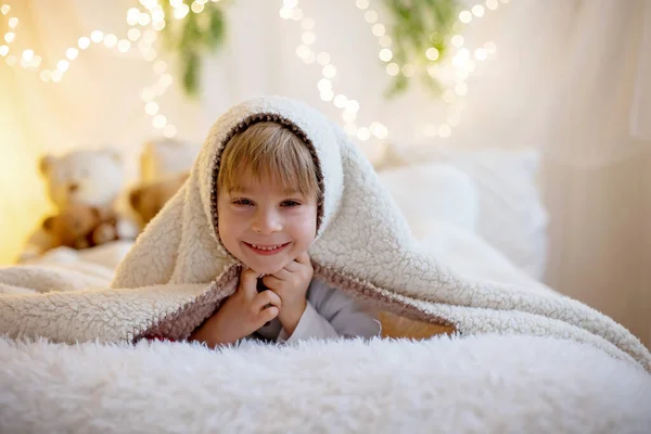 可爱的学龄前小男孩 抱着可爱的泰迪熊 躲在毯子下 在阳光灿烂的卧室里在家里玩耍 — 图库照片