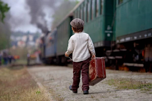 stock image Two boys, dressed in vintage clothing and hat, with suitcase, on a railway station