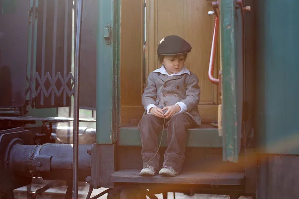 两个男孩穿着老式服装 头戴礼帽 提着手提箱 站在火车站上 — 图库照片