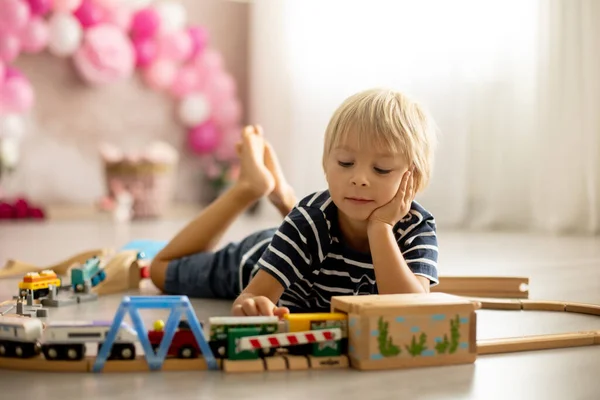 Cute child, blond toddler boy, playing with wooden trains at home