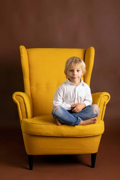 白いシャツの就学前の子供 カジュアルな服 孤立した背景に黄色のアームチェアに座って スタイリッシュな肖像画 — ストック写真