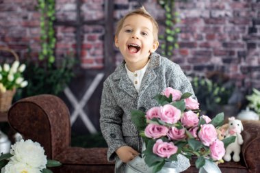 Şirin bir çocuk, beyaz gömlekli bir çocuk, Paskalya süslemesinde yumurta ve çikolatalı tavşanla oynuyor, stüdyo fotoğrafı.