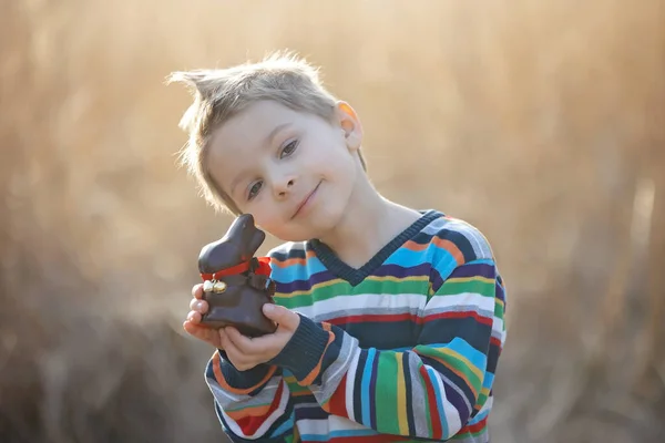 美しいスタイリッシュな幼児の子供 男の子 公園でイースターチョコレートウサギと遊ぶ — ストック写真