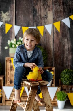 Sevimli bir anaokulu çocuğu, oğlum, evde ördeklerle oynuyor, arkasında doğum günü için güzel bir bahar süslemesi var.