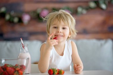 Tatlı çocuk, sarışın çocuk, smoothie içiyor ve evde çilek yiyor.