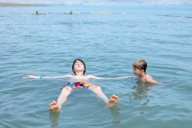 Çocuk, çocuk, çok sıcak bir yaz gününde Ölü denizde yüzüyor.