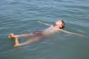 Çocuk, çocuk, çok sıcak bir yaz gününde Ölü denizde yüzüyor.