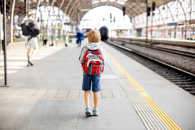 Sırt çantalı şirin anaokulu çocuğu, yaz mevsiminde tren istasyonunda koşuyor.