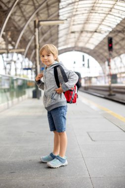 Sırt çantalı şirin anaokulu çocuğu, yaz mevsiminde tren istasyonunda koşuyor.