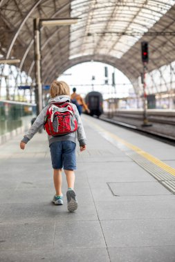 Sırt çantalı şirin anaokulu çocuğu, yaz mevsiminde tren istasyonunda koşuyor.