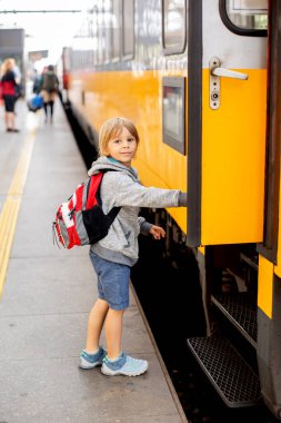 Sırt çantalı şirin anaokulu çocuğu, yaz mevsiminde tren istasyonunda koşuyor.