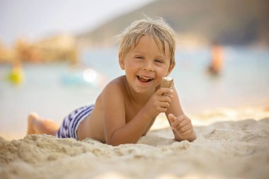 Happy child, boy eating ice cream  on the beach, enjoying summer, playing. Halkidiki, Greece
