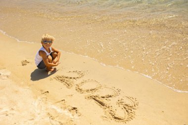 Child, cute boy, playing on the beach in the sand, enjoying summer, number sign