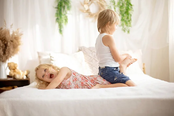 Cute sweet toddler children, tickling feet on the bed, laughing and smiling, childish mischief, happiness