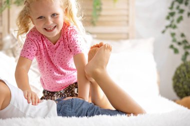 Sevimli küçük çocuklar, yatakta ayaklarını gıdıklıyor, gülüyor ve gülümsüyor, çocukça yaramazlıklar, mutluluk ve neşe