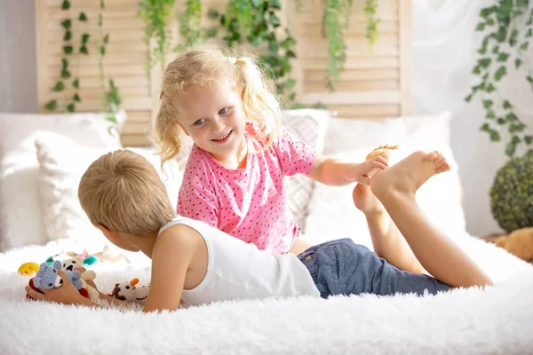 Cute sweet toddler children, tickling feet on the bed, laughing and smiling, childish mischief, happiness and joy