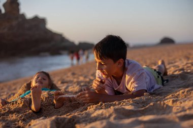 Çocuk, kumsalda ayaklarında tüyle gıdıklanan kardeş, çocuk kumla kaplı, gülümseyen, gülen, eğlenen