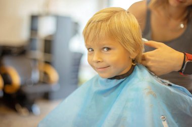 Cute toddler blond boy, having haircut in hairdresser salloon, smiling