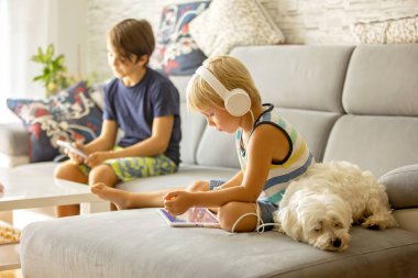 Sevimli çocuk, çocuk, evde tablette film izliyor, yanında tatlı bir Malta köpeği yatıyor.