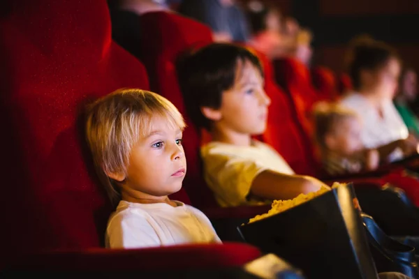 Cute child, boy, watching movie in a cinema, eating popcorn and enjoying the film