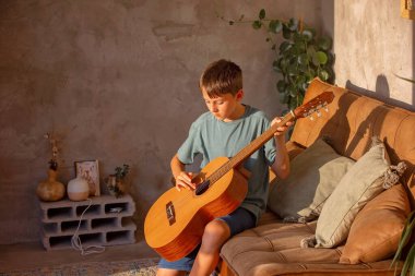 Çocuk, çocuk, evde akustik gitar çalmayı öğreniyor, güneşli bir odada.