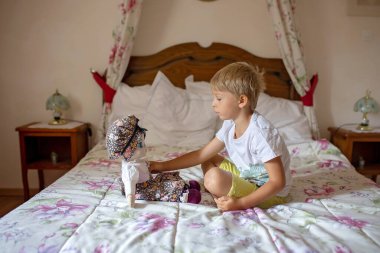 Sevimli sarışın çocuk, çocuk, evde oyuncaklarla, gemiyle, bebeklerle, otantik evle oynuyor.