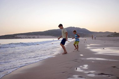Mutlu çocuklar, gün batımında sahilde oynuyorlar, çocuklar okyanusta koşuyor, mutlu bir çocukluk.