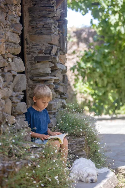 Beautiful medieval village Talasnal in Lousa, Portugal on a beautiful day. Child playing on the street of the village with his pet dog, reading book