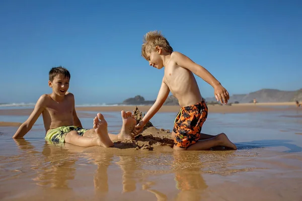 Child, tickling sibling on the beach on the feet with feather, kid cover in sand, smiling, laughing, enjoying some fun